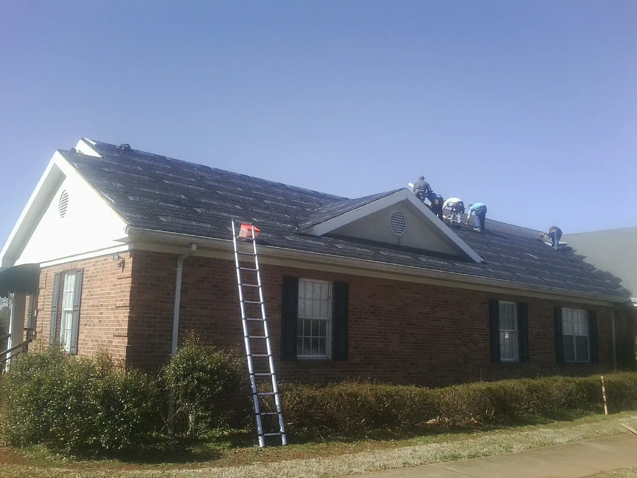Crew tearing shingles off a brick ranch roof with a ladder set — Emergency Roof Repair work by our crew in Sparta